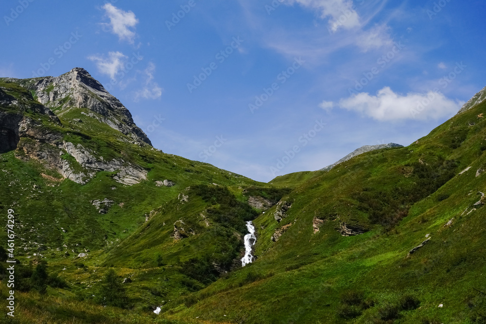 white waterfall in a green mountain landscape with blue sky