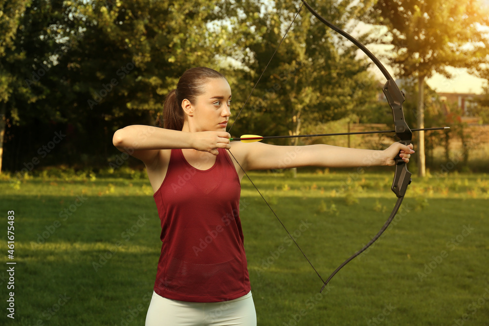 Woman with bow and arrow practicing archery in park Woman with bow and arrow practicing archery in park