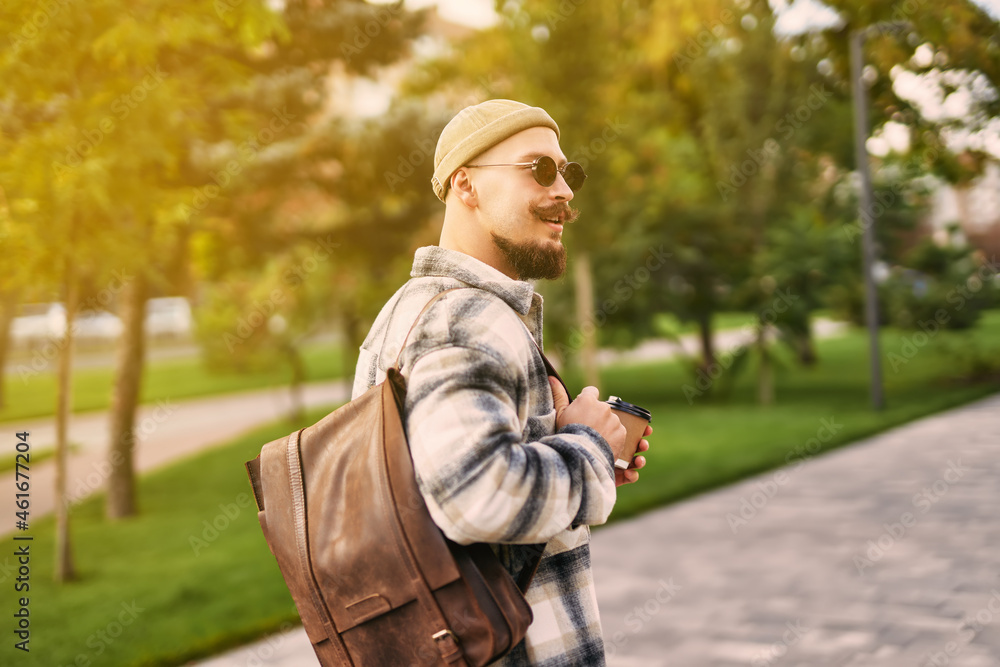 Back view of hipster bearded student looks sideways while walks in urban city park. Rest day Back view of hipster bearded student looks sideways while walks in urban city park. Rest day