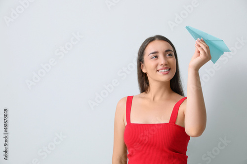 Beautiful young woman playing with paper plane on light grey background. Space for text