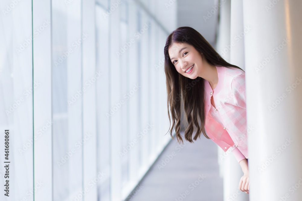 Beautiful teenage Asian girl wears a white with pink shirt and smiles cheerfully while she stands near the glassed window on a nice day. Beautiful teenage Asian girl wears a white with pink shirt and smiles cheerfully while she stands near the glassed window on a nice day.
