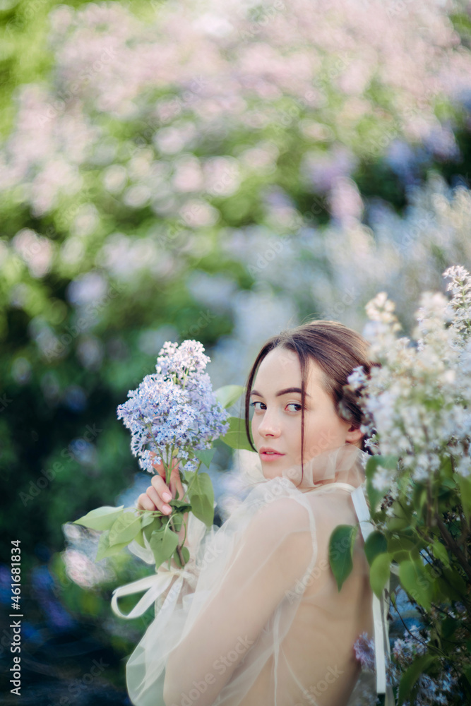 Naklejka premium Portrait of young woman in garden among blooming lilac shrubs.