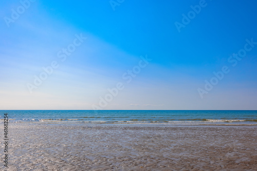 The waves of the ocean break onto the wet sandy beach  overlooked by a beautiful and clear blue sky