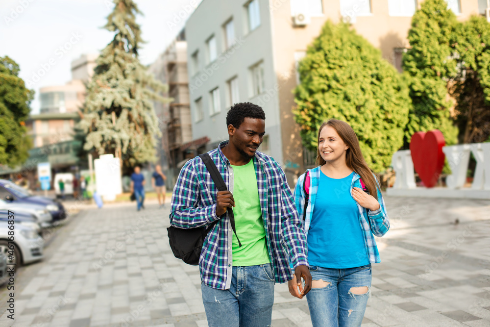 Two friends with backpacks walking and talking outdoors Two friends with backpacks walking and talking outdoors