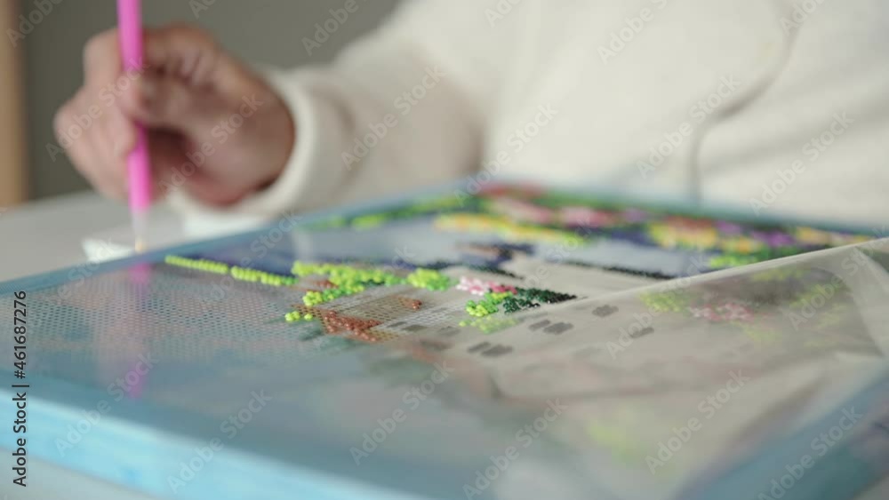Elderly woman in comfortable white woolen cardigan spends free time laying out diamond embroidery carefully extreme closeup Elderly woman in comfortable white woolen cardigan spends free time laying out diamond embroidery carefully extreme closeup
