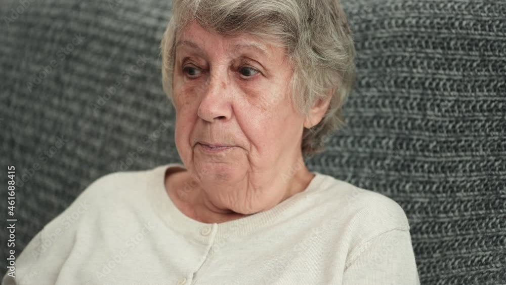 Portrait of old dissatisfied woman with gray hair and wrinkled face talking emotionally sitting on sofa covered with blanket closeup Portrait of old dissatisfied woman with gray hair and wrinkled face talking emotionally sitting on sofa covered with blanket closeup