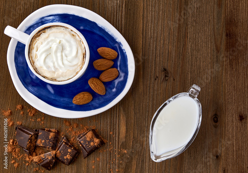 Blue cup of cappuccino, almonds, chocolate and milk in a glass milk jug