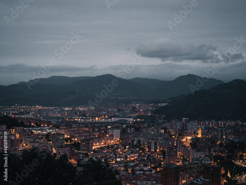Night photography from a viewpoint; Bilbao illuminated at night. Views of Bizkaia at dusk. Nature, darkness, clouds and mountains in dark Bilbao.