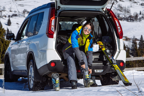 woman changing boots to ski sitting in car trunk. sunny day