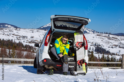 Photography man sitting in car trunk changing for snowboard