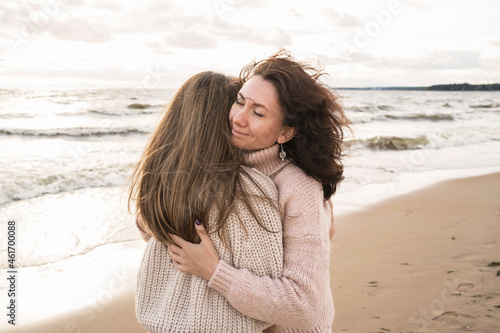Cozy autumn walk of two girls on the shore of the windy sea. Adult sisters are trarking in blankets from the wind. A couple in love walks down the street and hugs
