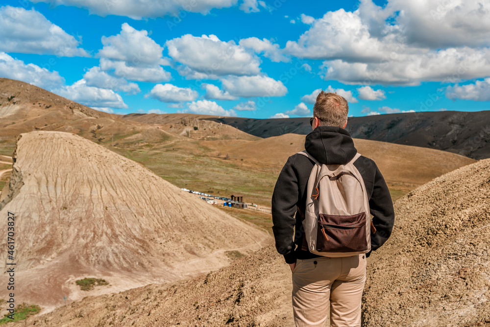  A young man with a backpack stands on top of a mountain overlooking the hills above Cape Chameleon in Crimea. The concept of tourism and mountain climbing.