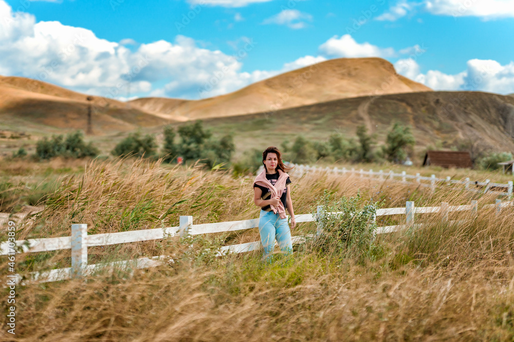 Naklejka premium A charming young woman at a white rustic style fence and a view of hills and mountains
