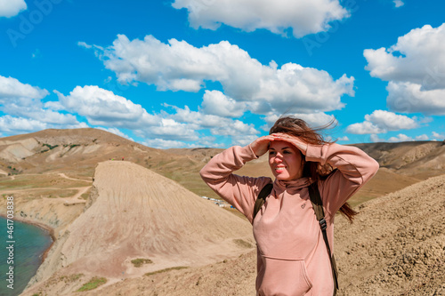 A young woman with a backpack stands on top of a mountain overlooking the hills above Cape Chameleon in Crimea. The concept of tourism and mountain climbing.