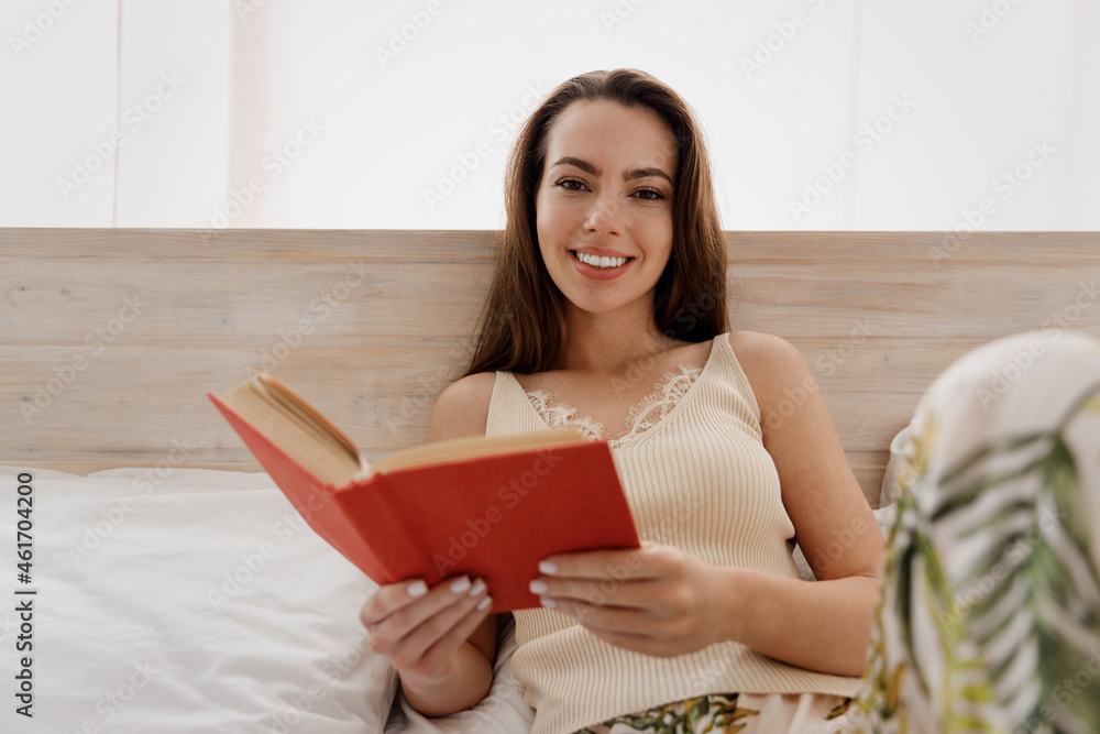 Close up charming marvelous young woman in casual casual clothes lay on bed holding reading book look camera rest relax spend time in bedroom lounge home in own room house be lost in reverie good day. Close up charming marvelous young woman in casual casual clothes lay on bed holding reading book look camera rest relax spend time in bedroom lounge home in own room house be lost in reverie good day.