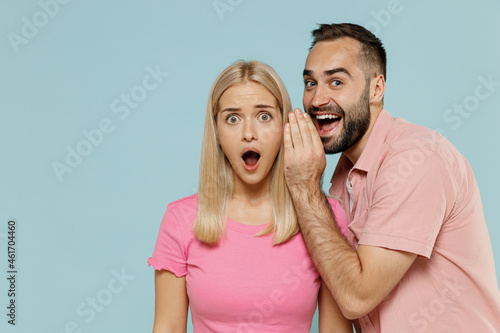 Young couple two friends family man surprised woman wear casual clothes whisper gossip tell secret behind her hand sharing news together isolated on pastel plain light blue color background studio