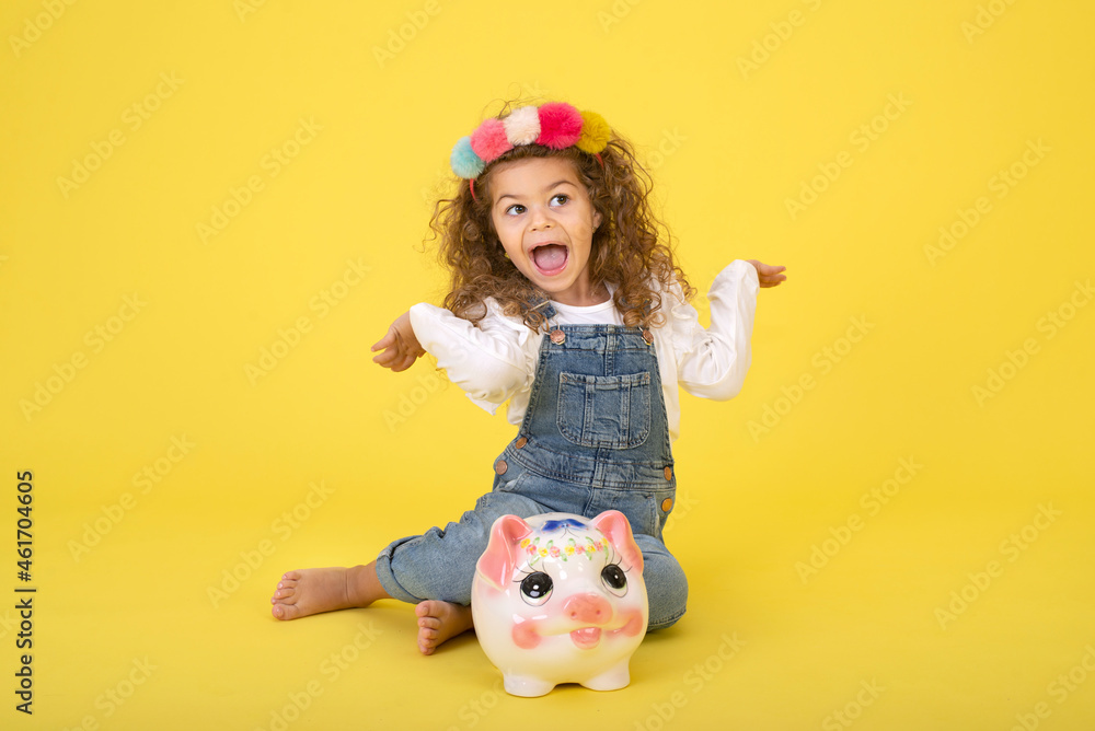Happy  Little Children girl  saved a little money for future need wearing white T-shirt holding piggy bank, Saving money since childhood on yellow background  studio shot with copy space