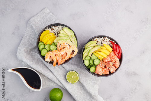 Poke bowl with salmon,shrimps, avocado, rice, cucumber, mango, pepper and sesame seeds, soy sauce on grey background. Hawaiian ahi, a diet meal with with seafood. Top view.