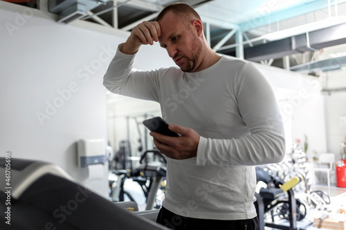 Cropped shot of a Caucasian male in early 30s running on treadmill during his workout and checking smart phone. Young man using mobile phone while exercising on treadmill. Healthy Lifestyle.