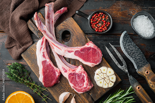 Raw lamb chops or mutton cuts, with ingredients carrot orange, herbs, on old dark  wooden table background, top view flat lay