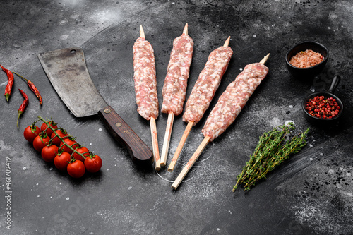 Raw Lula kebab on skewers, with grill ingredients, on black dark stone table background, with copy space for text