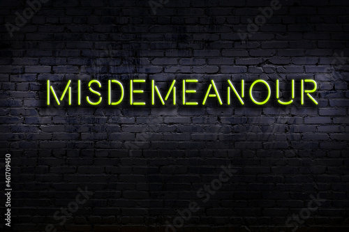 Fotografie Neon sign. Word misdemeanour against brick wall. Night view
