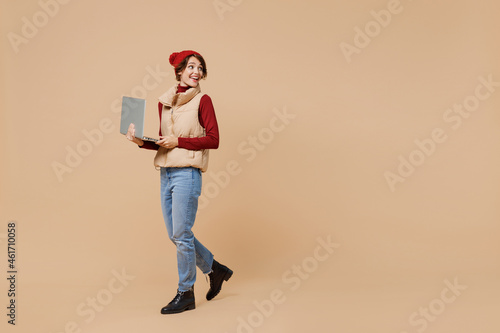 Εκτύπωση καμβά Full body side view young woman 20s wears red turtleneck vest beret hold use work on laptop pc compute look aside isolated on plain pastel beige background studio portrait
