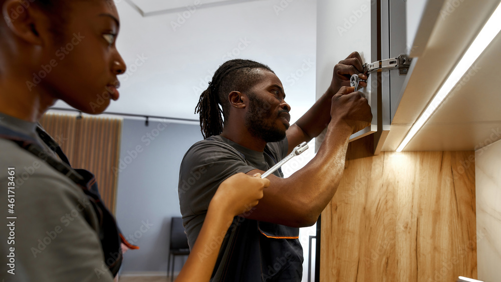 Young female apprentice watching skilled handyman installing cupboard Young female apprentice watching skilled handyman installing cupboard