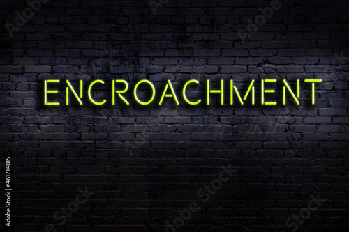 Night view of neon sign on brick wall with inscription encroachment