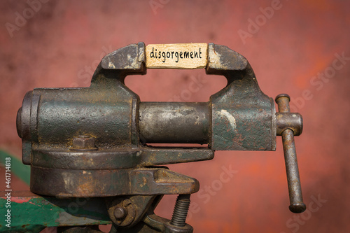 Vice grip tool squeezing a plank with the word disgorgement photo