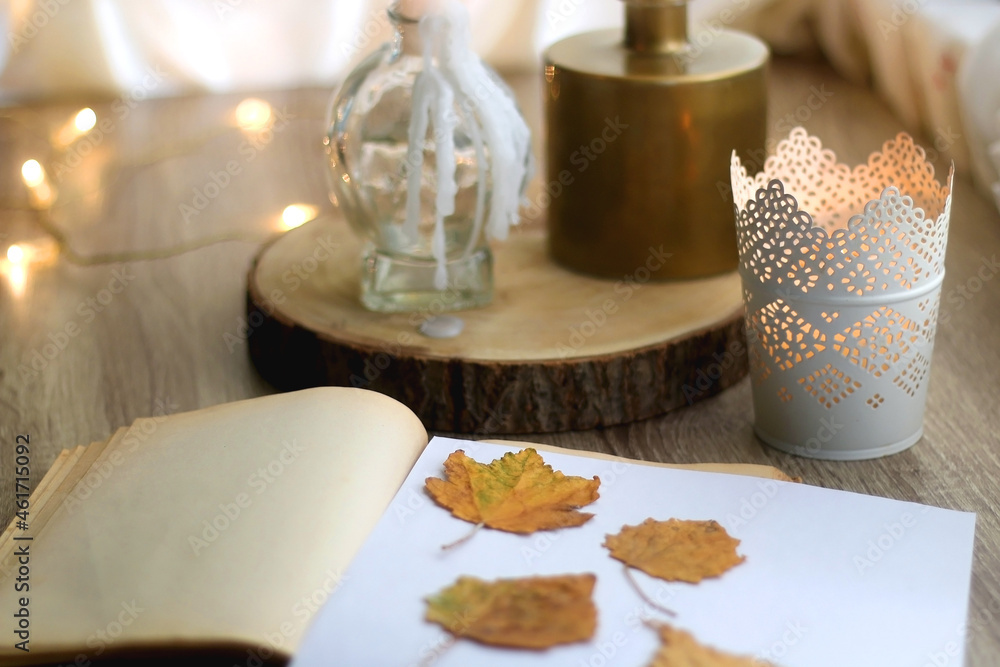 Old book with pressed autumn leaves, lit candles and vase with gypsophila flowers. Selective focus. Old book with pressed autumn leaves, lit candles and vase with gypsophila flowers. Selective focus.