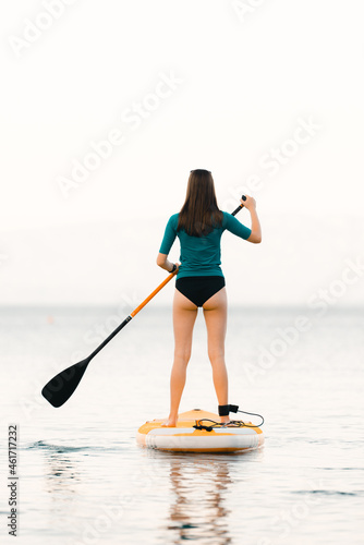 Young girl on a paddle-board with a paddle in her hand - shot from the back, calm surface of the sea - copy space