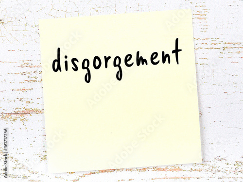 Yellow sticky note on wooden wall with handwritten word disgorgement photo