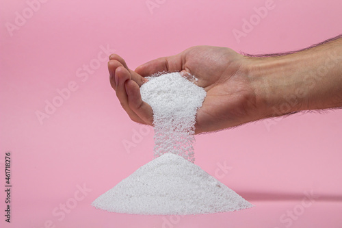 Washing powder on a pink background. Detergent for washing clothes. Washing powder pouring out of a man's hand photo