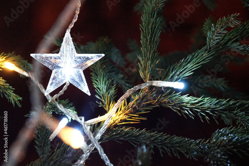 White lights on the Christmas tree. Star shaped decoration. Bright Christmas Eve in dark night.