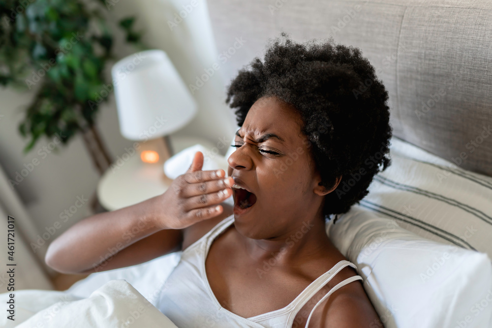 beautiful young African woman in tank top lying in bed yawn in the morning