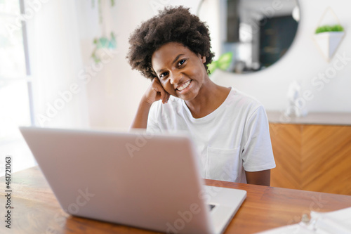 Smiling young African female entrepreneur working online with a laptop while sitting at her kitchen table at home photo