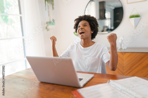 Smiling young African female entrepreneur working online with a laptop while sitting at her kitchen table at home photo