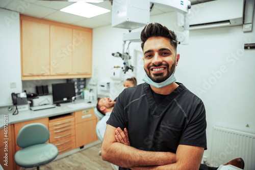 Mixed race male nurse smiling with arms crossed standing in dentist room with female colleague and client 