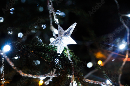 White lights on the Christmas tree. Star shaped decoration. Bright Christmas Eve in dark night.
