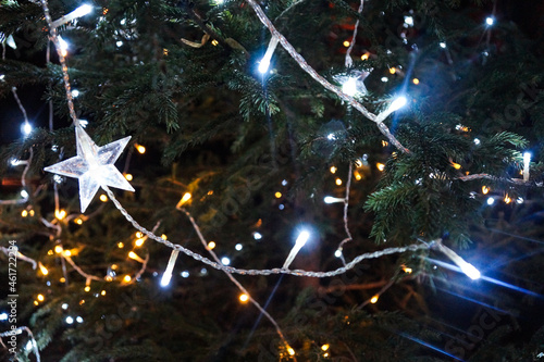 White lights on the Christmas tree. Star shaped decoration. Bright Christmas Eve in dark night.