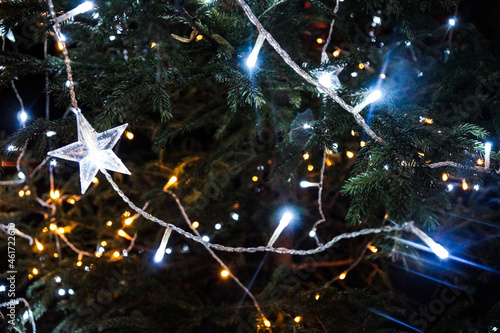 White lights on the Christmas tree. Star shaped decoration. Bright Christmas Eve in dark night.
