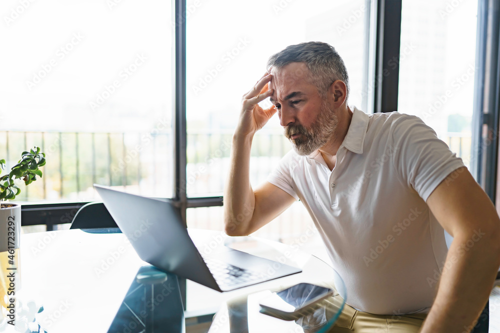 Fototapeta premium Businessman sitting at desk in bright office using laptop with sad attitude