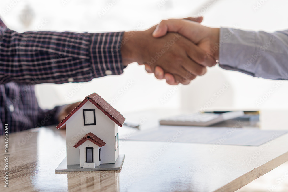 A handshake between the sales representative and the landlord when signing a home purchase or renting contact at the workspace desk. A real estate agent or bank officer explains the interest on a loan