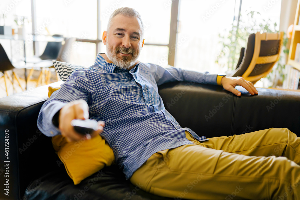 Foto Stock mature man with remote control watching tv at home | Adobe Stock