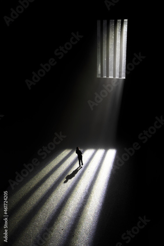 silhouette of a mysterious person walking in the shadow facing bars and daylight in a moody surrounding.