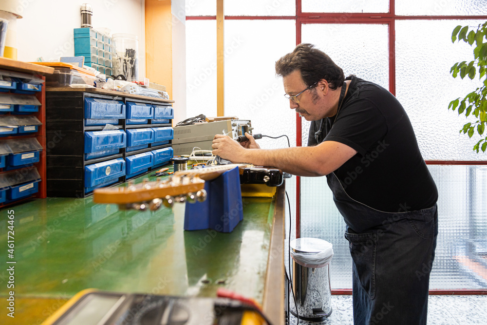 Serious man repairing guitar in workshop Serious man repairing guitar in workshop