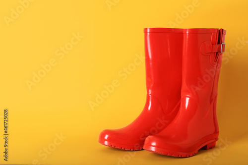 Pair of red rubber boots on orange background. Space for text