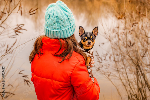 A girl in a winter jacket and a hat with her back to the camera with a dog. Pet and owner.