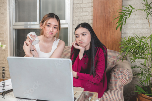 Two friends watch a boring movie streaming on the laptop while sitting on the couch. photo